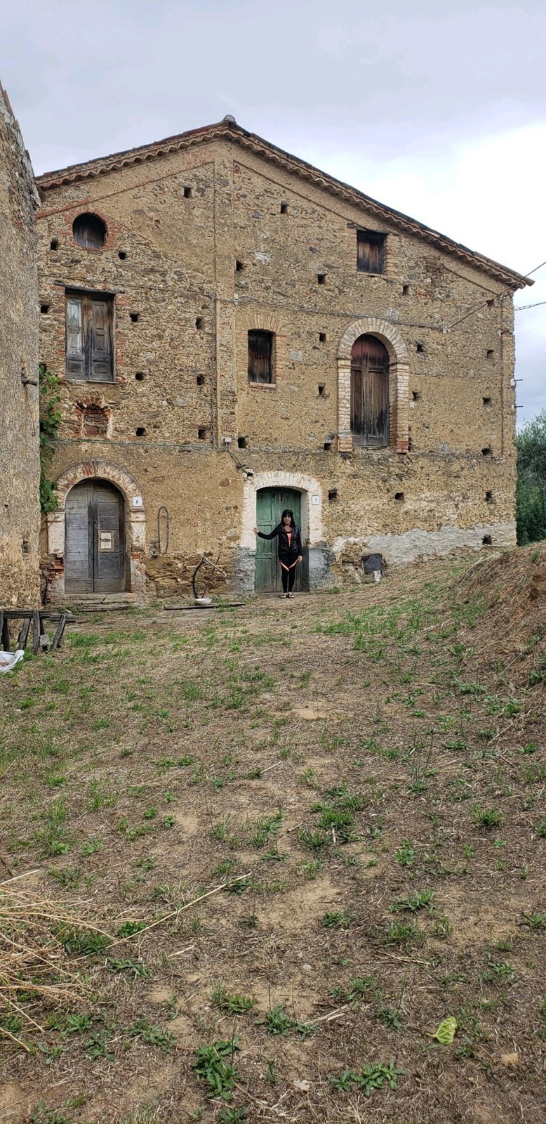 A tan stone house with arched wooden doors and a woman standing in a green doorway
