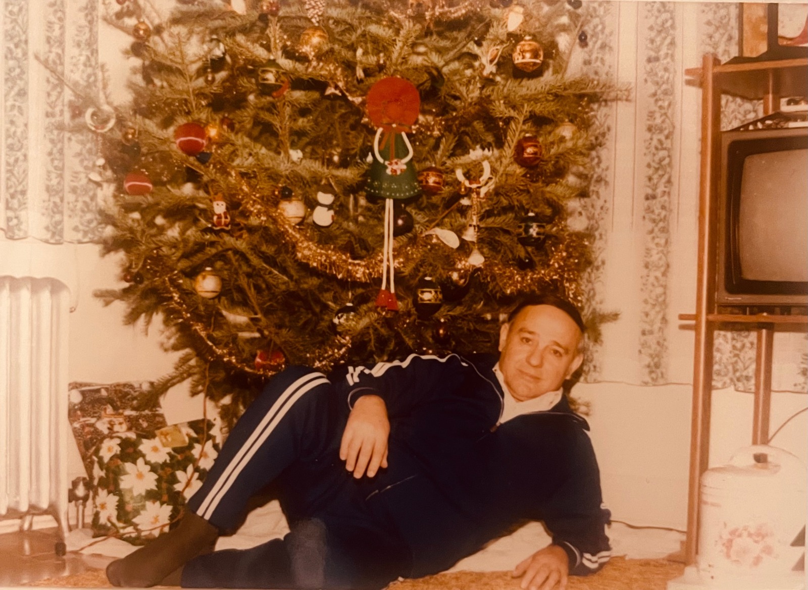 A man resting on the floor in front of a decorated Christmas tree