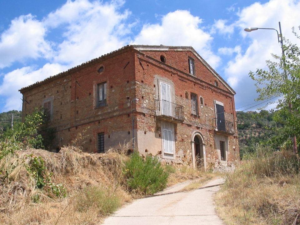 A red brick house standing alone on a hillside lane in Calabria, Italy