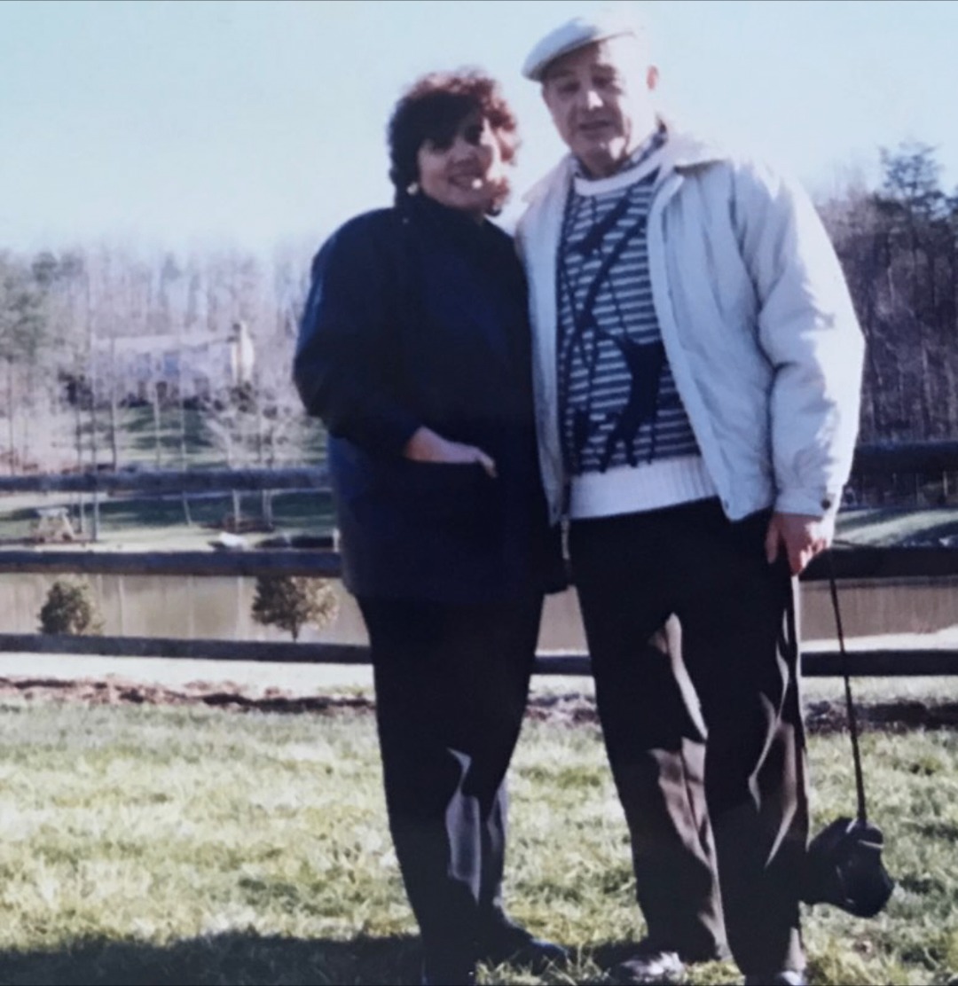 An older couple standing arm in arm on a grassy field on a clear day