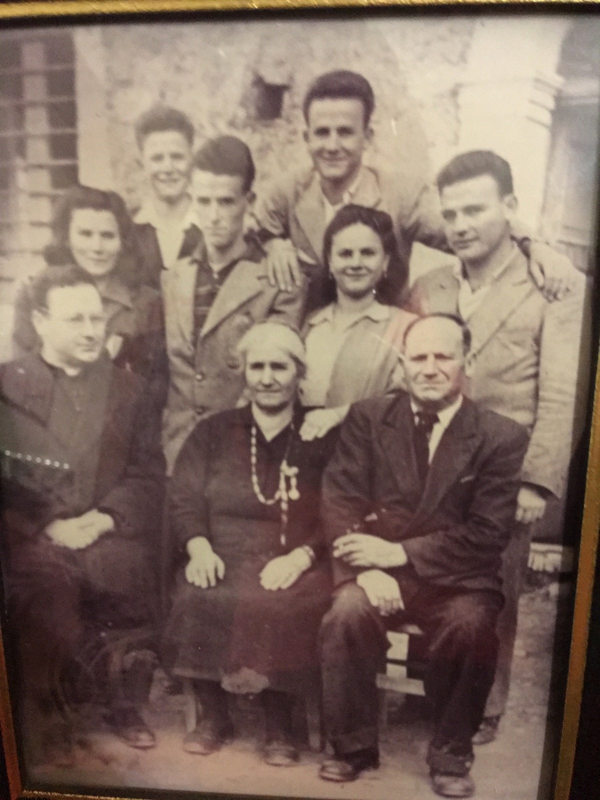 An old framed sepia portrait of a large group posed outside a stone house